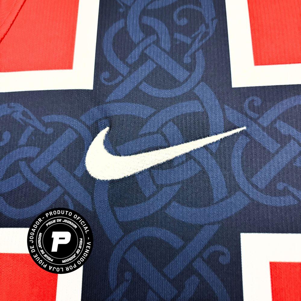 Camisa Nike Noruega 26/27 Home, , PIQUE DE JOGADOR, A Camisa Noruega 2026 Home representa o uniforme principal da seleção da Noruega para o ciclo da Copa do Mundo de 2026, trazendo um design moderno com forte inspiração na identidade nacional do país. O modelo apresenta a tradicional base em vermelho, cor histórica da seleção norueguesa, combinada com uma releitura marcante da bandeira do país. Um grande cruzamento em azul marinho com contornos brancos percorre o peito e o corpo da camisa, criando um visual