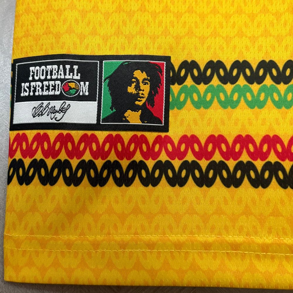 Camisa Adidas Jamaica 26/27 Home, , PIQUE DE JOGADOR, A Camisa Adidas Jamaica 26/27 Home representa o uniforme principal da seleção jamaicana para o ciclo da Copa do Mundo de 2026, trazendo um dos designs mais criativos e culturais do futebol atual. Inspirada diretamente na cultura reggae e no legado de Bob Marley, a camisa apresenta uma base em amarelo vibrante com padrões horizontais em verde, vermelho e dourado. Esses elementos fazem referência às cores tradicionais da Jamaica e ao estilo icônico do arti