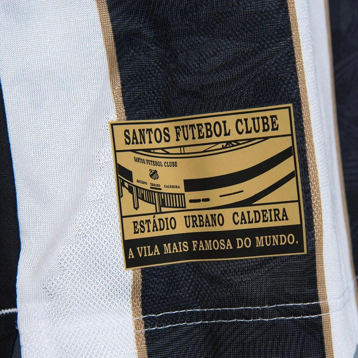 Camisa Masculina Umbro Santos 2024/25 II Jogador S/N, Camisas de Futebol, Umbro, A nova camisa reserva do Santos para 2024/25 traz de volta o tradicional listrado preto e branco em um design moderno e cheio de personalidade. Com listras verticais detalhadas por finas linhas douradas, o manto carrega símbolos gráficos em alto relevo que homenageiam a história do Peixe. Na versão jogador, o modelo entrega leveza, caimento atlético e tecnologia de ponta, exatamente como usado pelos atletas em campo. Especifica