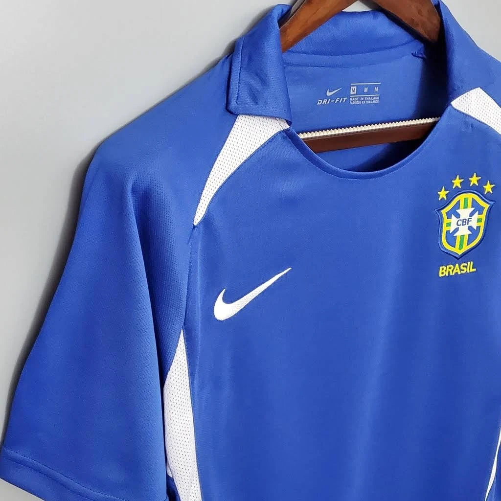 Camisa Retrô Seleção Brasilileira 2002 Away, Camisas de Futebol, PIQUE DE JOGADOR, Reviva um dos momentos mais gloriosos da história do futebol brasileiro com a Camisa Retrô Seleção Brasileira 2002 Away. Inspirada no uniforme reserva utilizado pela Seleção na campanha do pentacampeonato mundial, essa camisa representa a conquista histórica que consagrou o Brasil como a única seleção com cinco títulos da Copa do Mundo. O modelo em azul clássico ficou marcado nas partidas em que a Seleção precisou utilizar o 