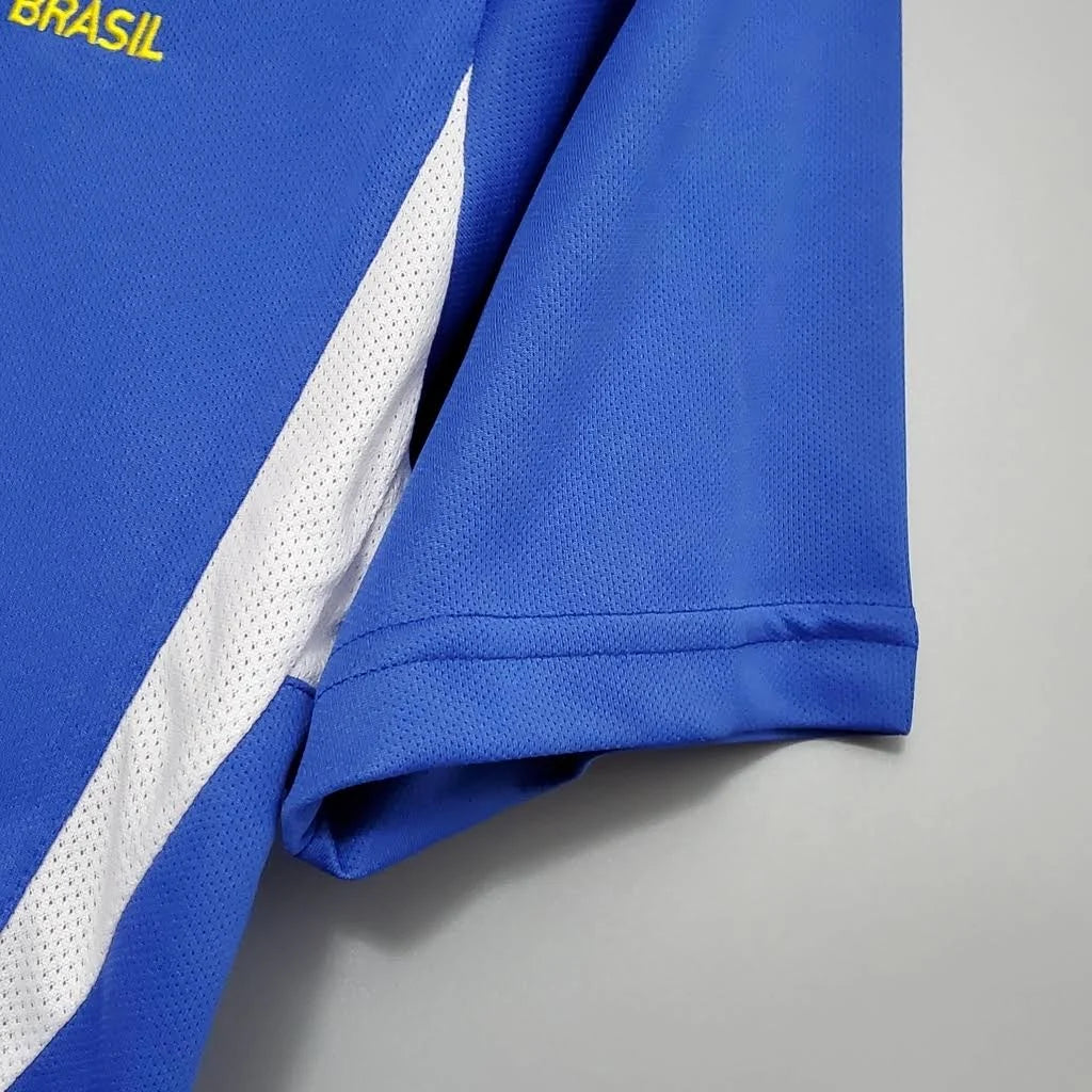 Camisa Retrô Seleção Brasilileira 2002 Away, Camisas de Futebol, PIQUE DE JOGADOR, Reviva um dos momentos mais gloriosos da história do futebol brasileiro com a Camisa Retrô Seleção Brasileira 2002 Away. Inspirada no uniforme reserva utilizado pela Seleção na campanha do pentacampeonato mundial, essa camisa representa a conquista histórica que consagrou o Brasil como a única seleção com cinco títulos da Copa do Mundo. O modelo em azul clássico ficou marcado nas partidas em que a Seleção precisou utilizar o 