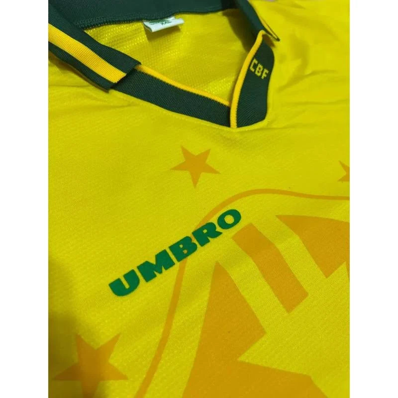 Camisa Umbro Retrô Seleção Brasil 1994 Home, Camisas de Futebol, PIQUE DE JOGADOR, Reviva um dos capítulos mais gloriosos do futebol brasileiro com a Camisa Umbro Retrô Seleção Brasil 1994 Home. Inspirada no uniforme titular utilizado pela Seleção Brasileira na histórica campanha da Copa do Mundo de 1994, essa camisa representa o momento em que o Brasil conquistou seu tetracampeonato mundial. O design clássico em amarelo com detalhes verdes segue o estilo marcante da Umbro na época, trazendo elementos que s